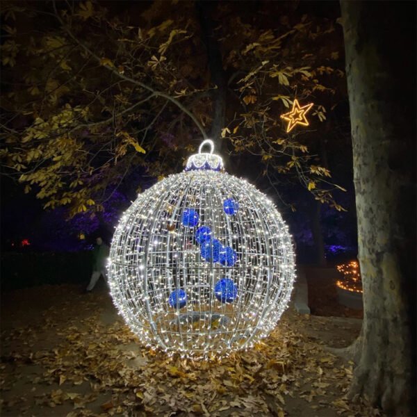 Illuminated round Christmas ornament arranged beside decorated trees in a night garden