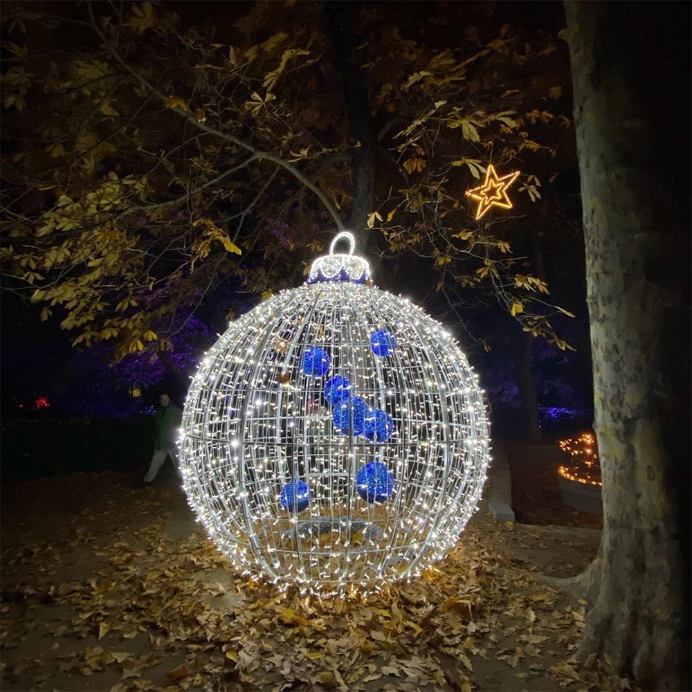 Illuminated round Christmas ornament arranged beside decorated trees in a night garden