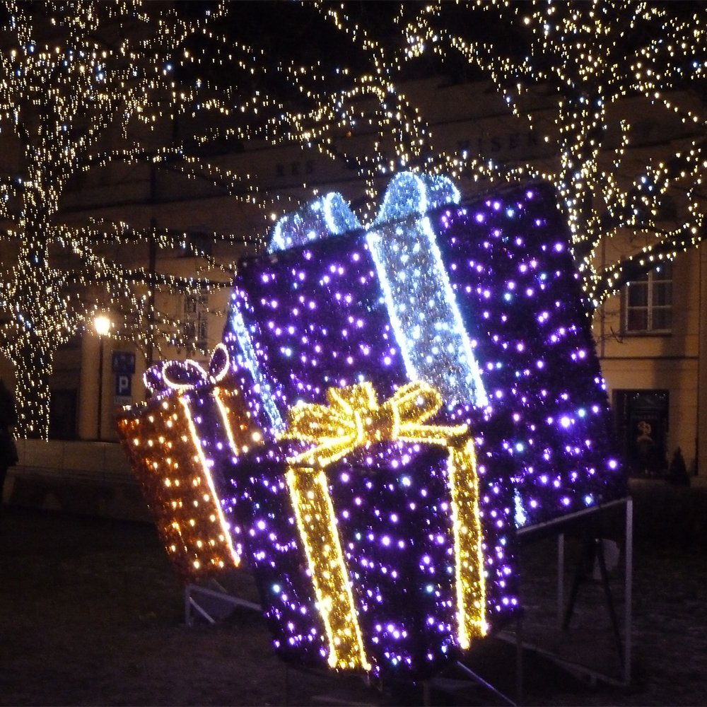 Layered illuminated gift boxes with contrasting bows in a festive town square
