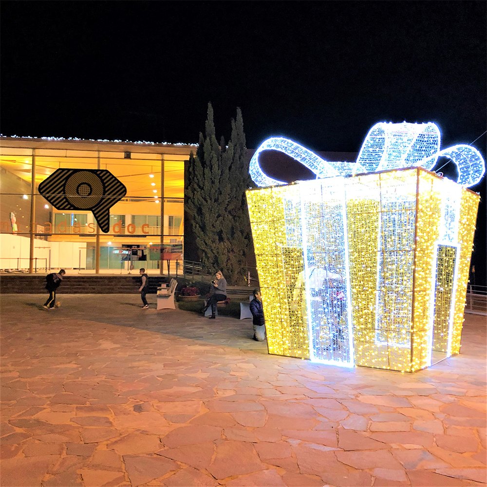 Illuminated gift pavilion with white loop bow and warm white walls in a public square