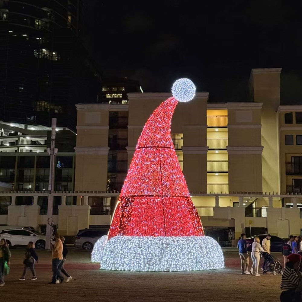 Giant illuminated Santa hat with a white rim and pom-pom in an open plaza