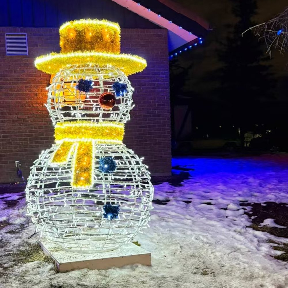 Illuminated open-frame snowman with a gold top hat and scarf beside a snowy building