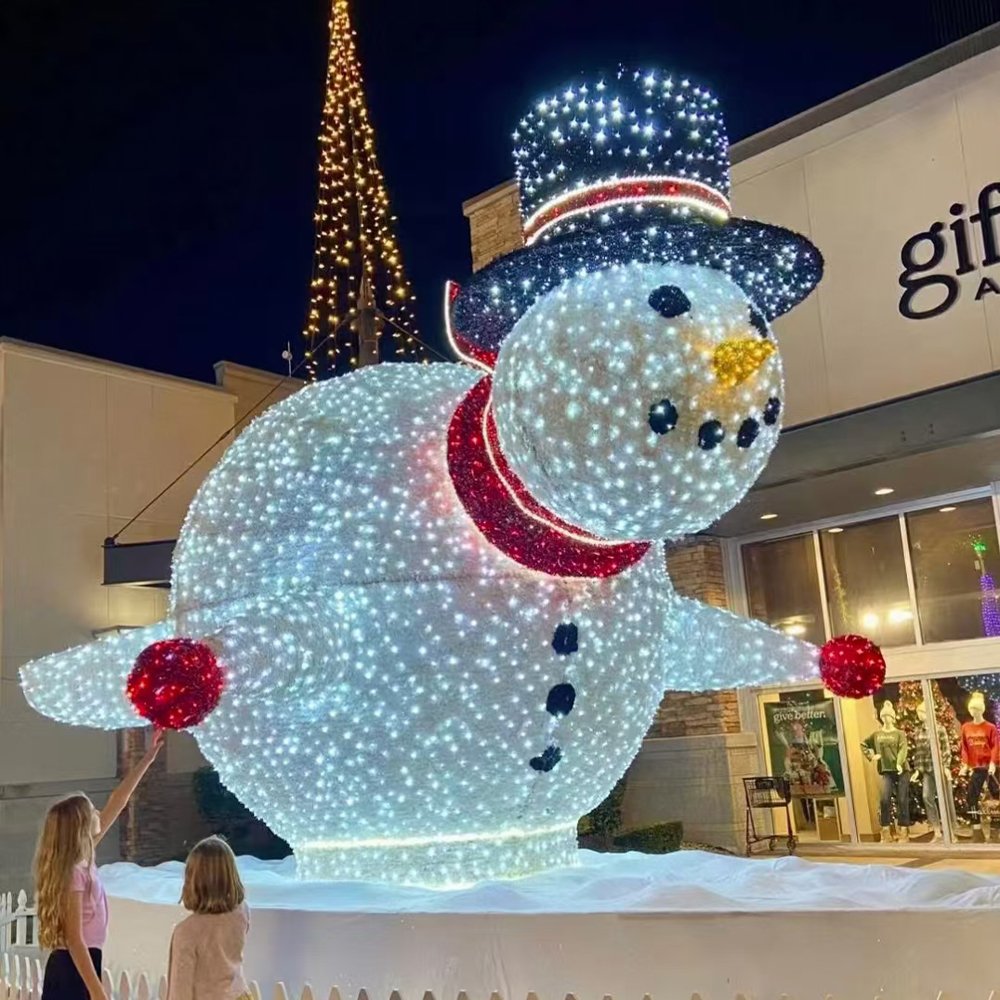 White illuminated snowman with a blue hat, red scarf and raised arm in a festive display