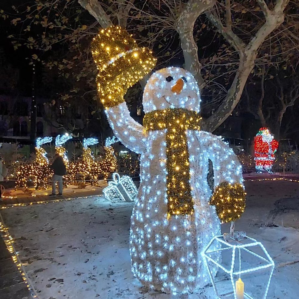 Illuminated smiling snowman raising a golden hat and carrying an outlined lantern beside a winter garden path