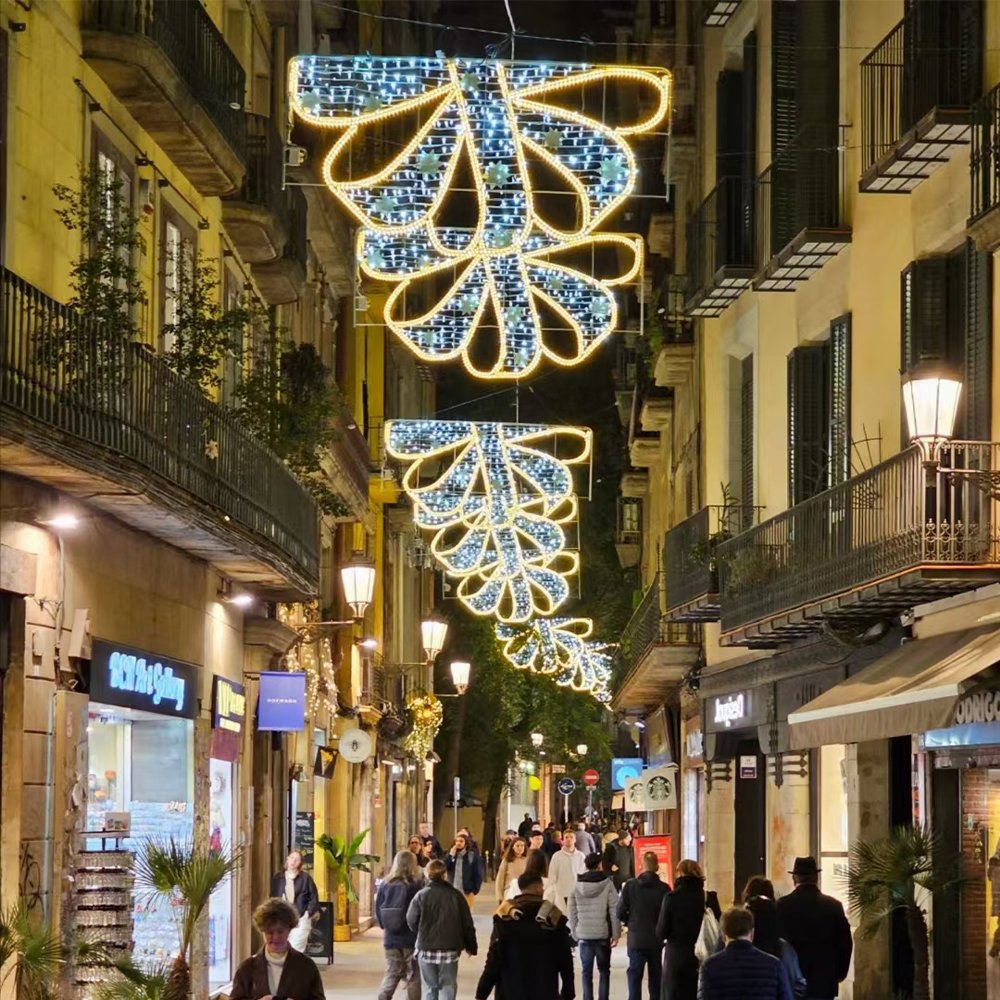 Suspended looping ribbon light motifs with pale illuminated fill and warm white outlines above a narrow shopping street