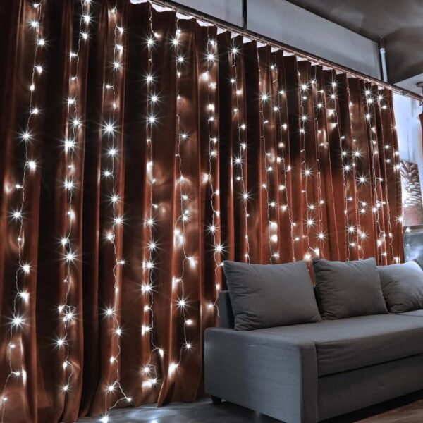 White curtain LED strands against dark brown fabric drapes behind a grey lounge sofa