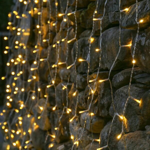 Close view of warm white LED drops on transparent twisted curtain cable against rough stone masonry