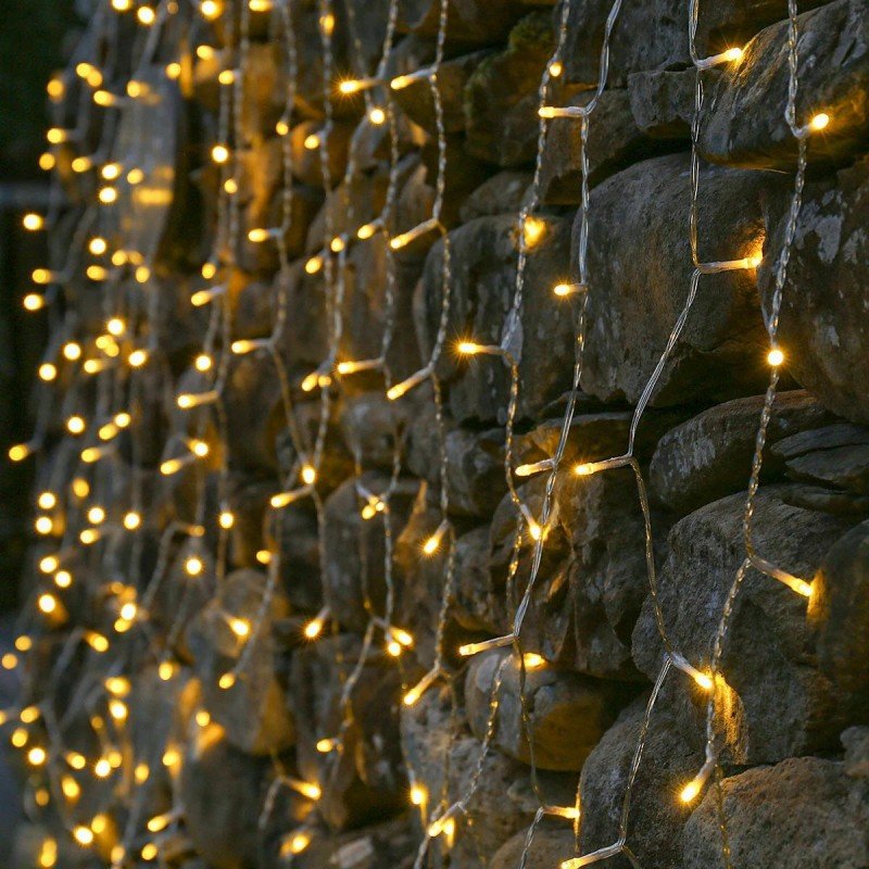 Close view of warm white LED drops on transparent twisted curtain cable against rough stone masonry