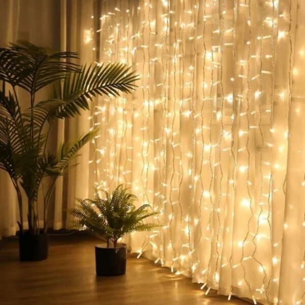 Warm white vertical curtain LEDs beside tall palm-like foliage and a smaller potted fern against cream drapes