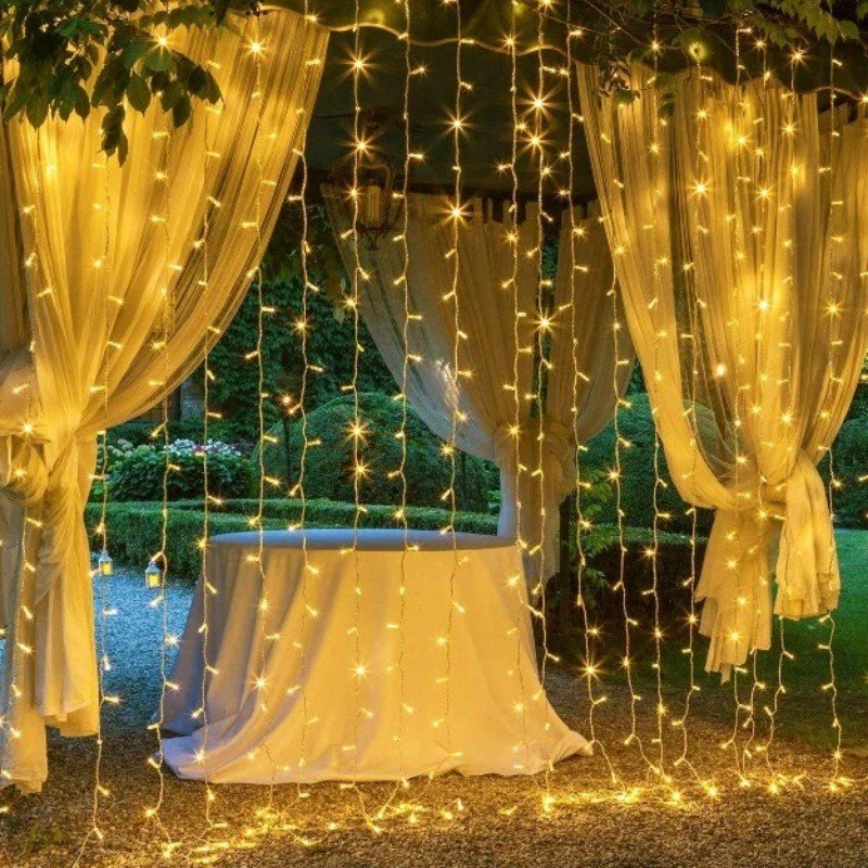 Warm white curtain strands framing tied-back sheer garden drapes and a cloth-covered reception table