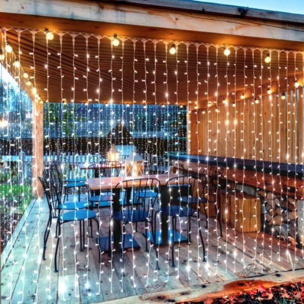 White-appearing curtain strands across the front of a timber dining deck with tables, dark chairs and lanterns