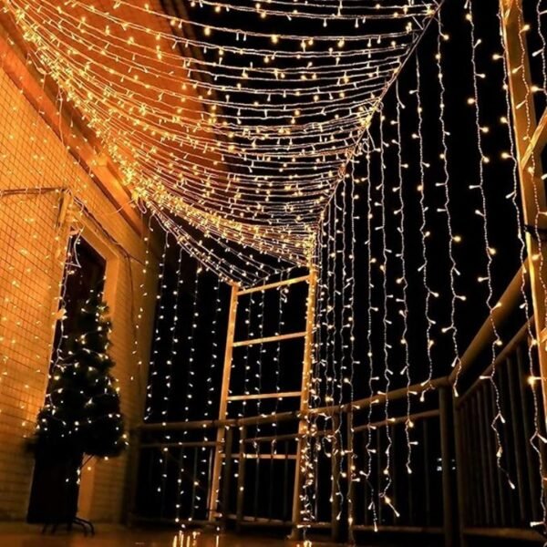 Warm white vertical curtain strands beside a terrace railing under overhead lights near a festive tree