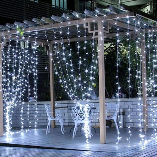 White curtain light strands draped beneath a pale pergola around ornamental garden chairs