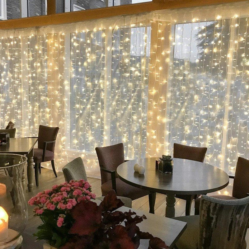 Warm white curtain string lights hanging across tall windows behind café tables and chairs