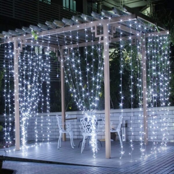 White curtain lights draped around a pale courtyard pergola with ornamental garden chairs