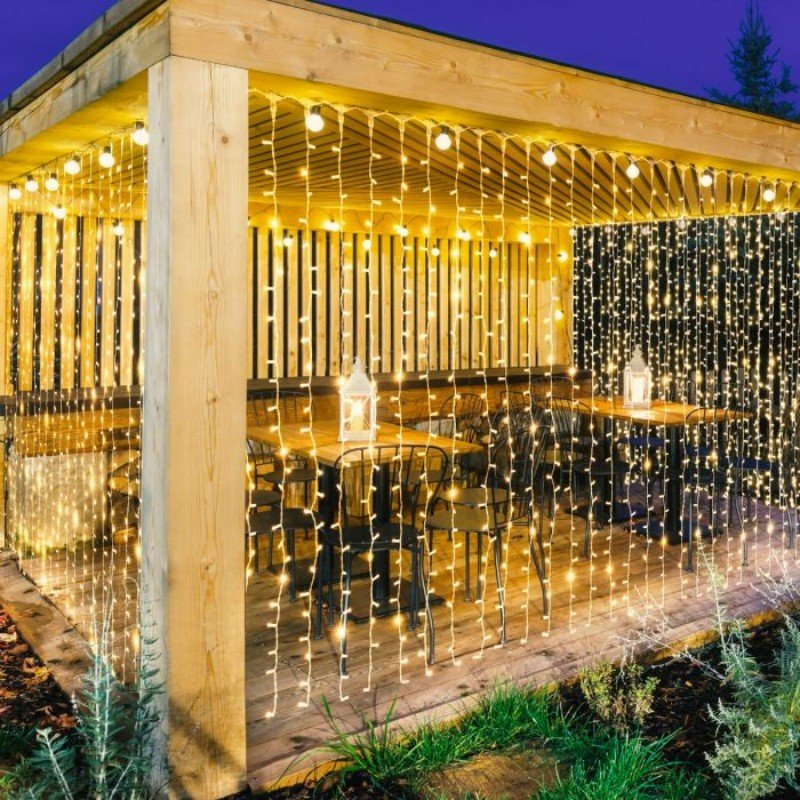 Warm white curtain lights around a timber cafe pavilion with dining tables and white lanterns