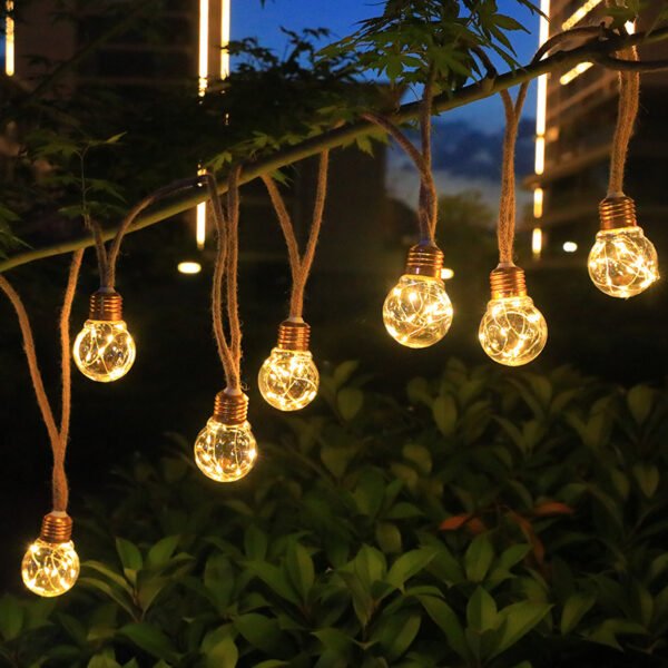 Clear round pendants glowing with warm pinpoint lights on rope-like drops beneath a leafy branch