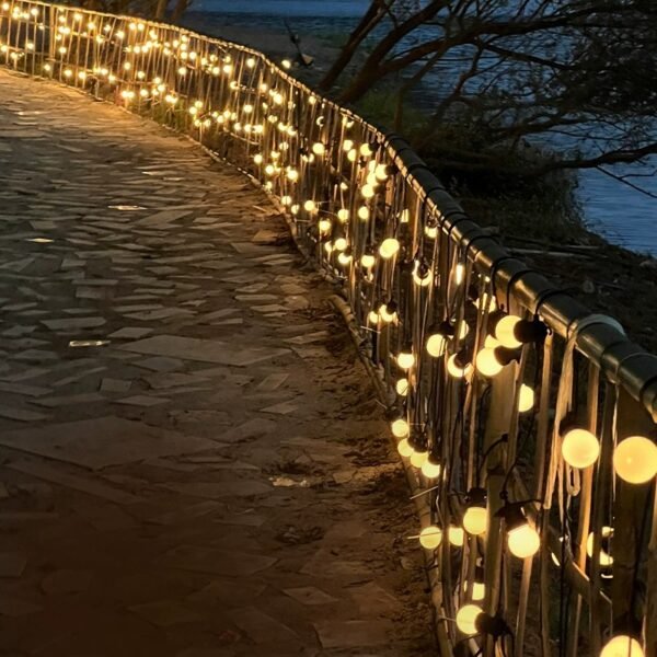 Warm white globe drops hanging along a curved railing beside a stone garden promenade at dusk