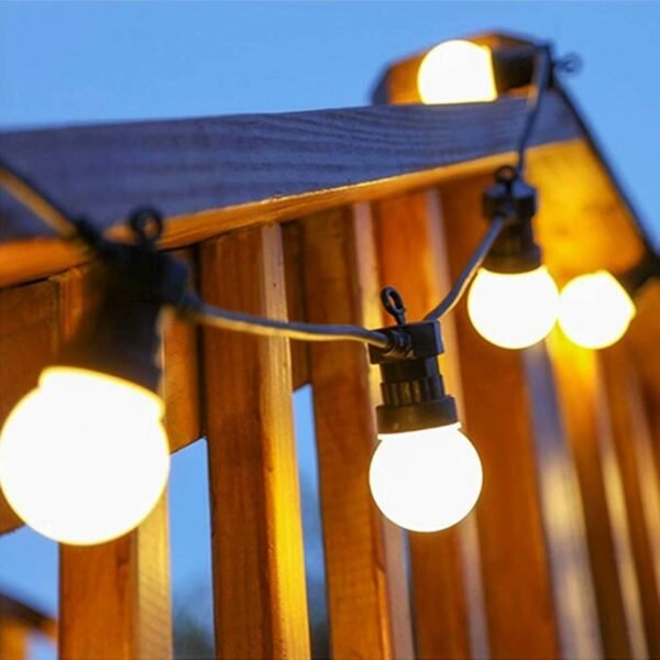 Warm white globe lights following a curved line beside vertical timber railing slats against a blue evening sky