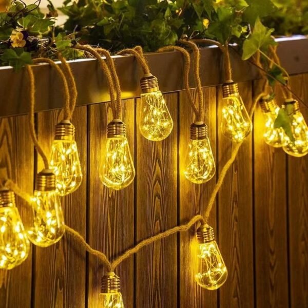 Warm white sparkling pear-shaped lights hanging at staggered positions before vertical timber boards beneath planting