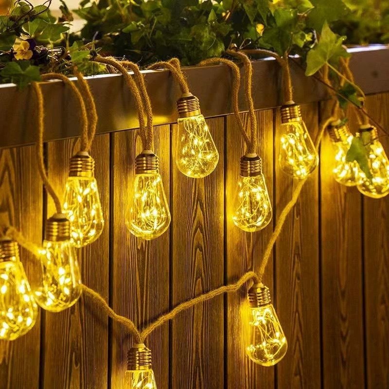Warm white sparkling pear-shaped lights hanging at staggered positions before vertical timber boards beneath planting