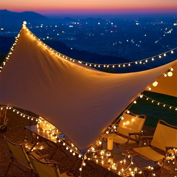 Warm white decorative light strands tracing a fabric canopy above camp chairs and tables overlooking a dusk landscape