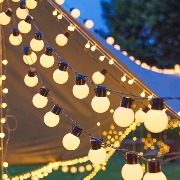Warm white round lights along a sloping fabric pavilion edge with further strands against a blue dusk sky
