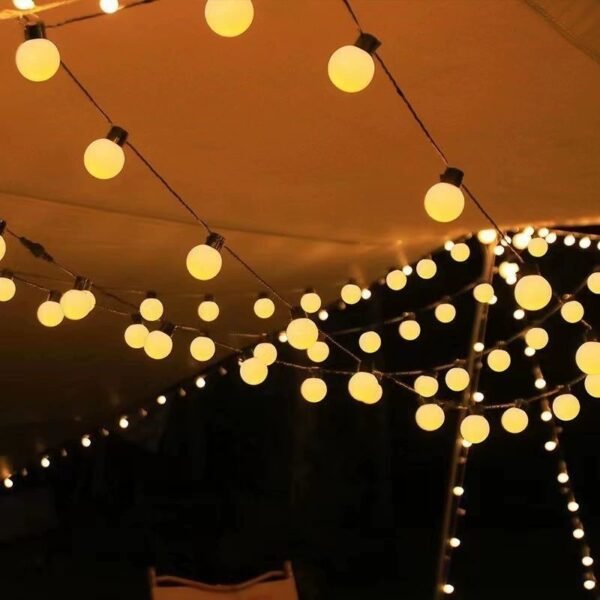 Warm white round Edison lights crossing beneath a fabric canopy around a vertical support at night