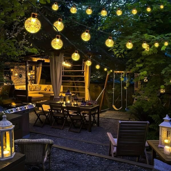 Warm white globe-shaped Edison lights above a garden dining table beside timber seating and leafy trees