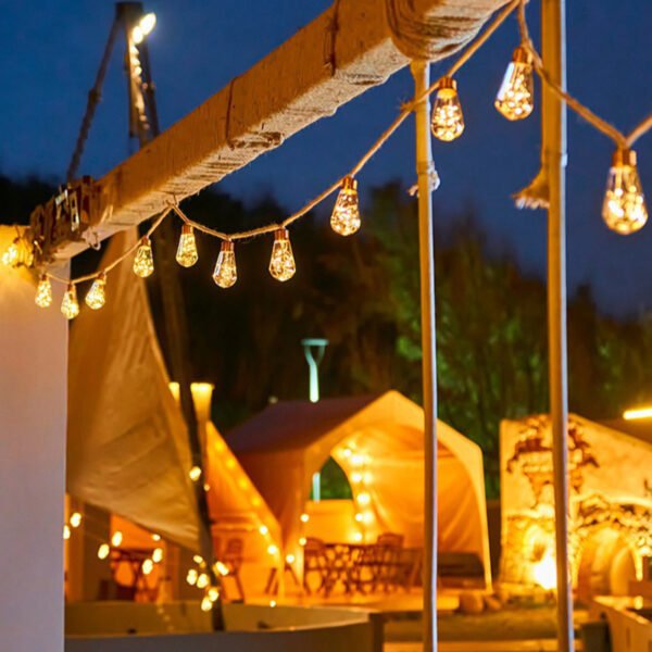 Warm pear Edison string lights following the edge of a tented hospitality area with illuminated camping tents behind